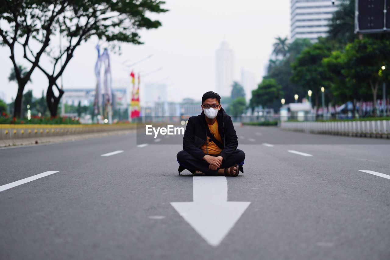 Portrait of man standing on road in city against corona virus