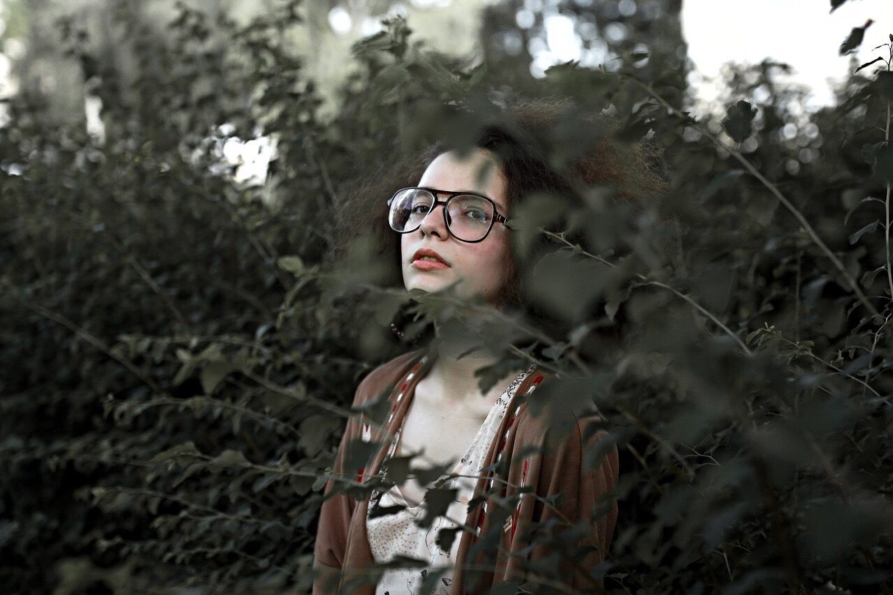 PORTRAIT OF YOUNG WOMAN STANDING AGAINST TREE