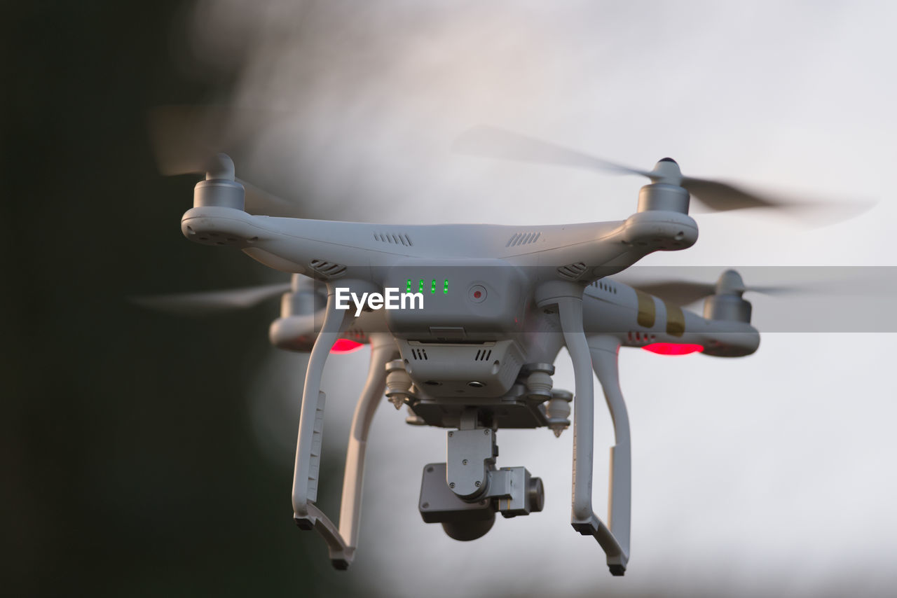 Drone quadcopter hovering in front of trees and blue sky, selective focus blurs the background