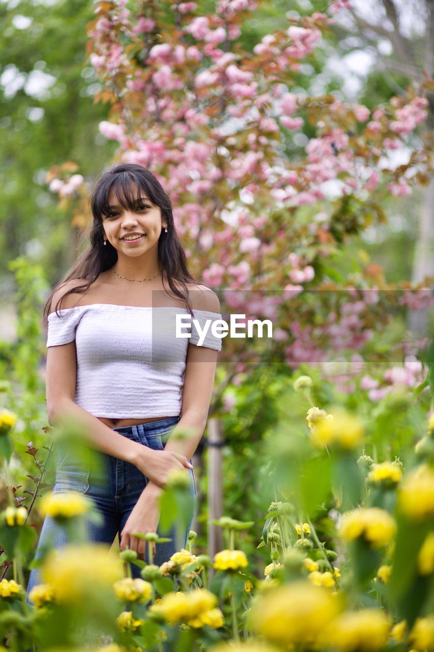 YOUNG WOMAN STANDING AGAINST PLANTS