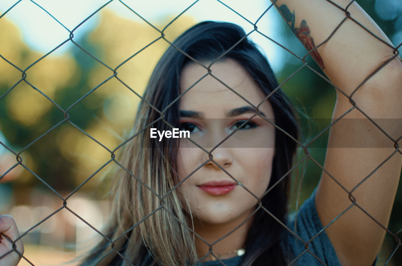 PORTRAIT OF BEAUTIFUL YOUNG WOMAN STANDING IN FENCE
