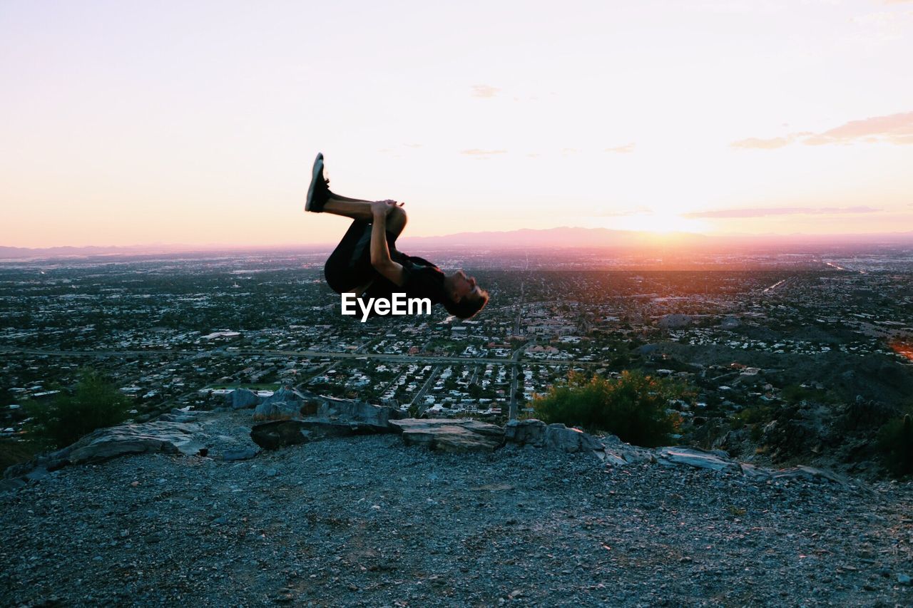 Full length of young man backflipping on mountain against sky during sunset