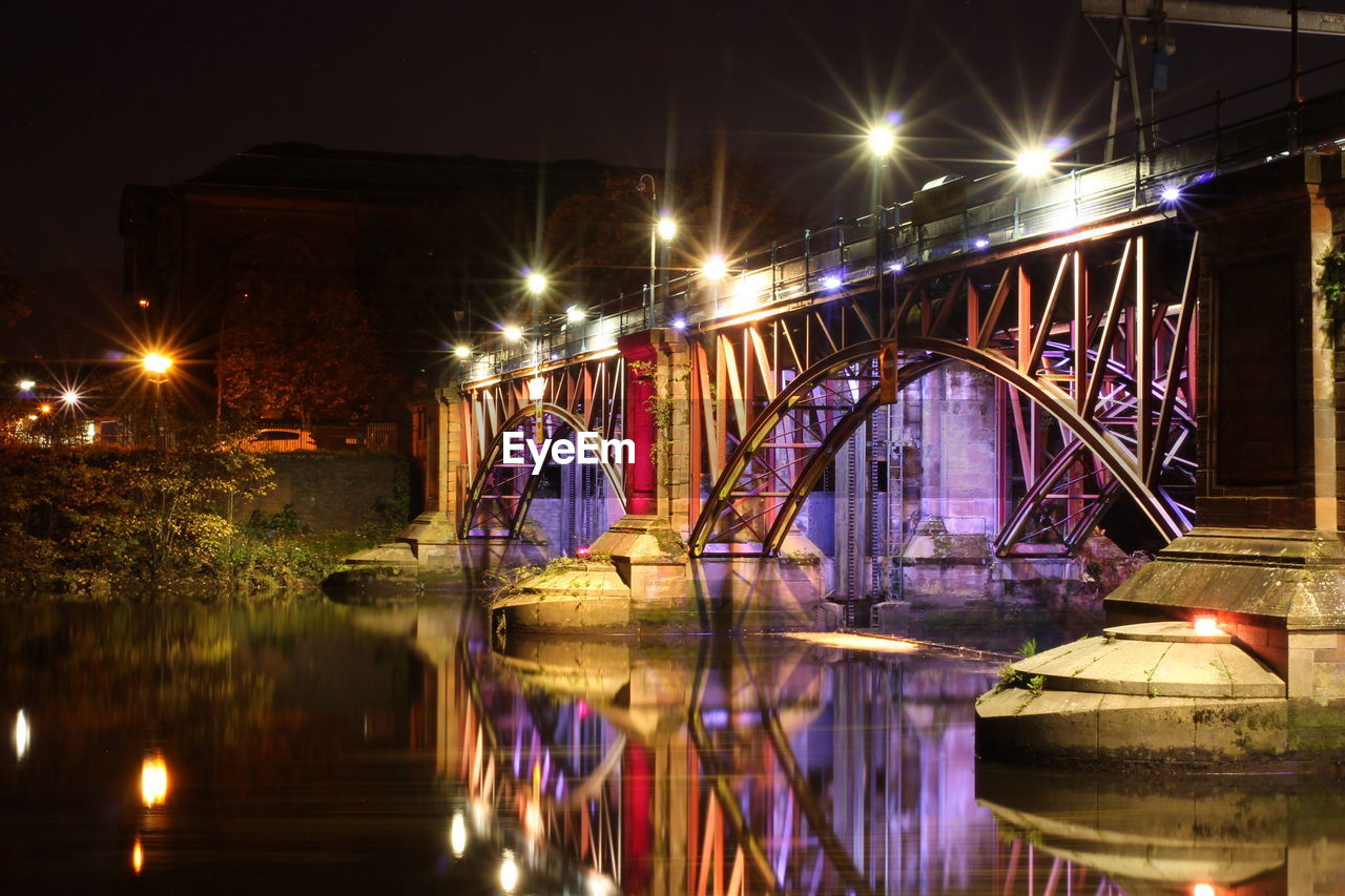 Illuminated bridge over river in city at night