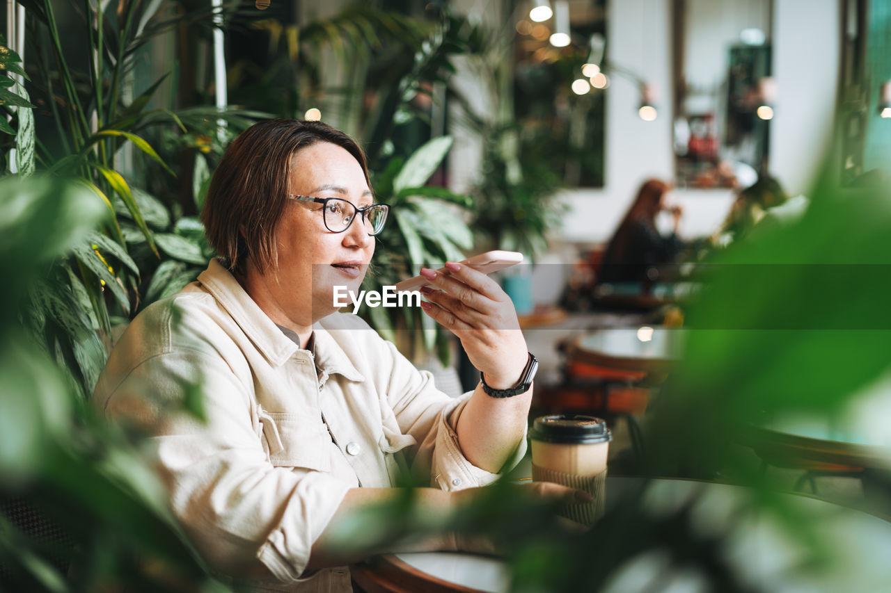 Adult middle aged woman plus size in casual clothes with coffee using mobile phone in cafe