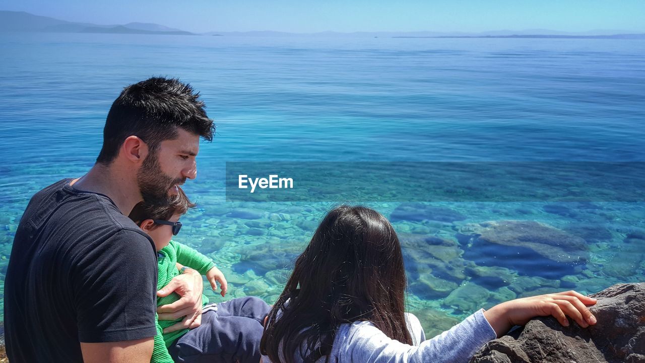 Father with children sitting by sea during sunny day