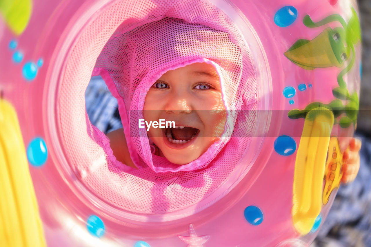 Close-up portrait of cute smiling girl with mouth open holding inflatable ring