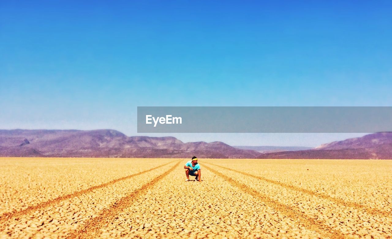 Man crouching on desert against clear blue sky