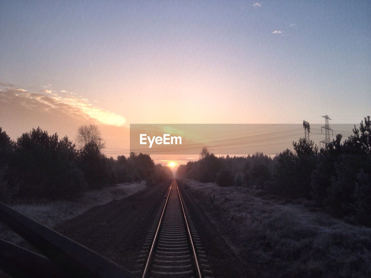 Silhouette trees amidst railroad track seen through train windshield at sunset