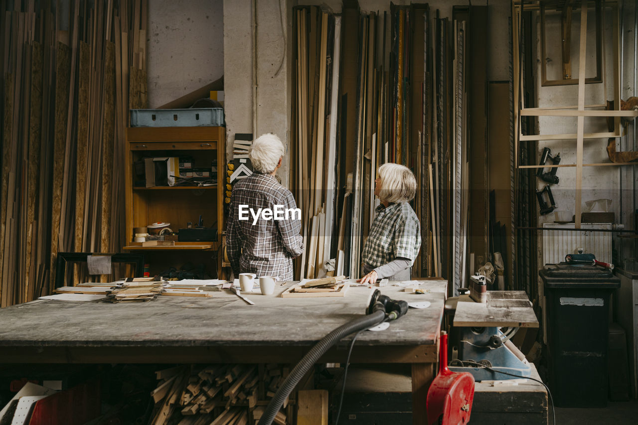 Male and female senior entrepreneurs looking at wood in workshop