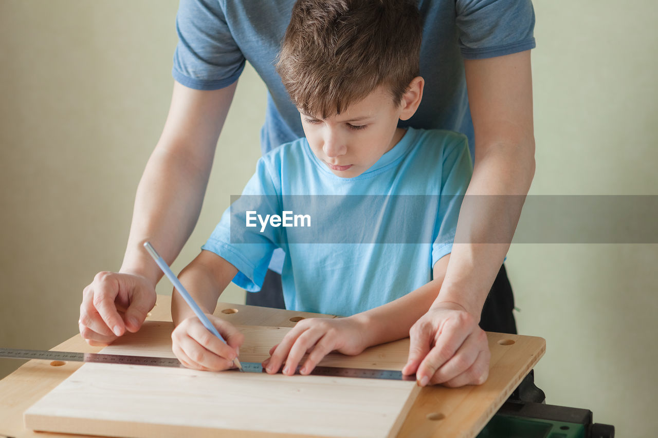 Father teaches son carpentry. cute little boy with pencil in hand making marks on wooden plank.