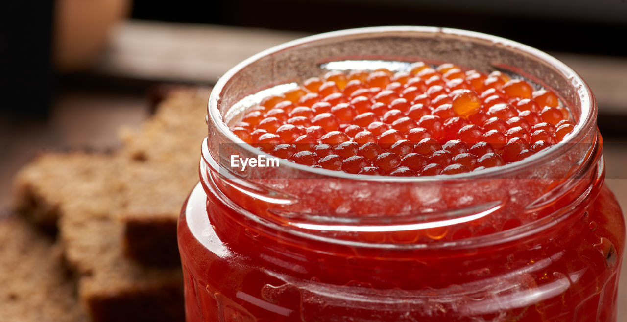 Full glass jar with red caviar on a brown wooden table, top view