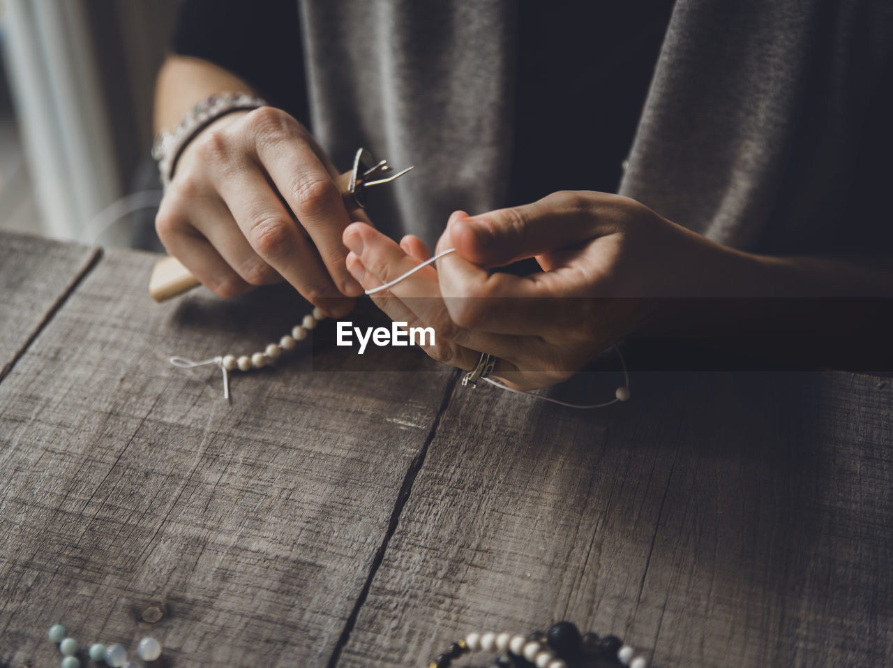 Close-up midsection of woman making bracelets at table