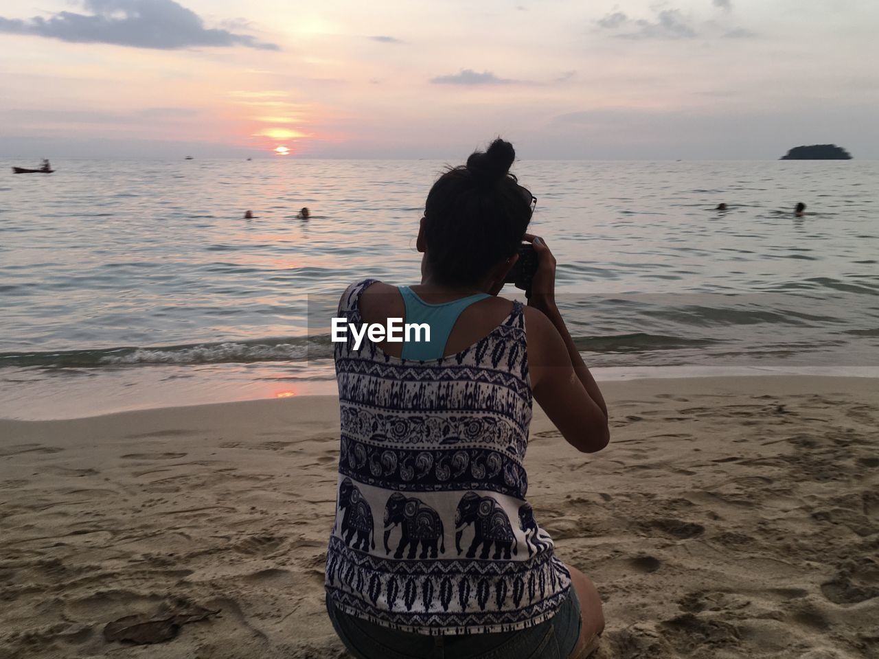 REAR VIEW OF WOMAN STANDING ON BEACH AT SUNSET