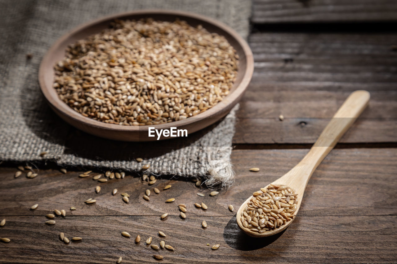 Flax seeds on wooden plate and wooden spoon on wooden base.