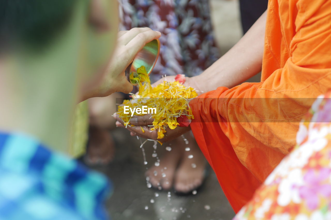 Man pouring water on hands of person carrying flower petals