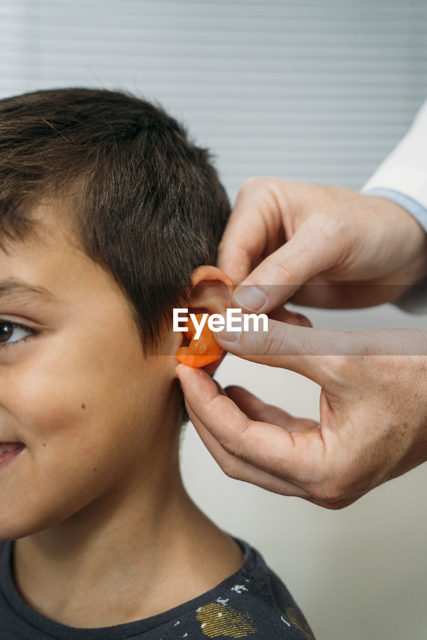 Male audiologist putting hearing air in child's ear at clinic