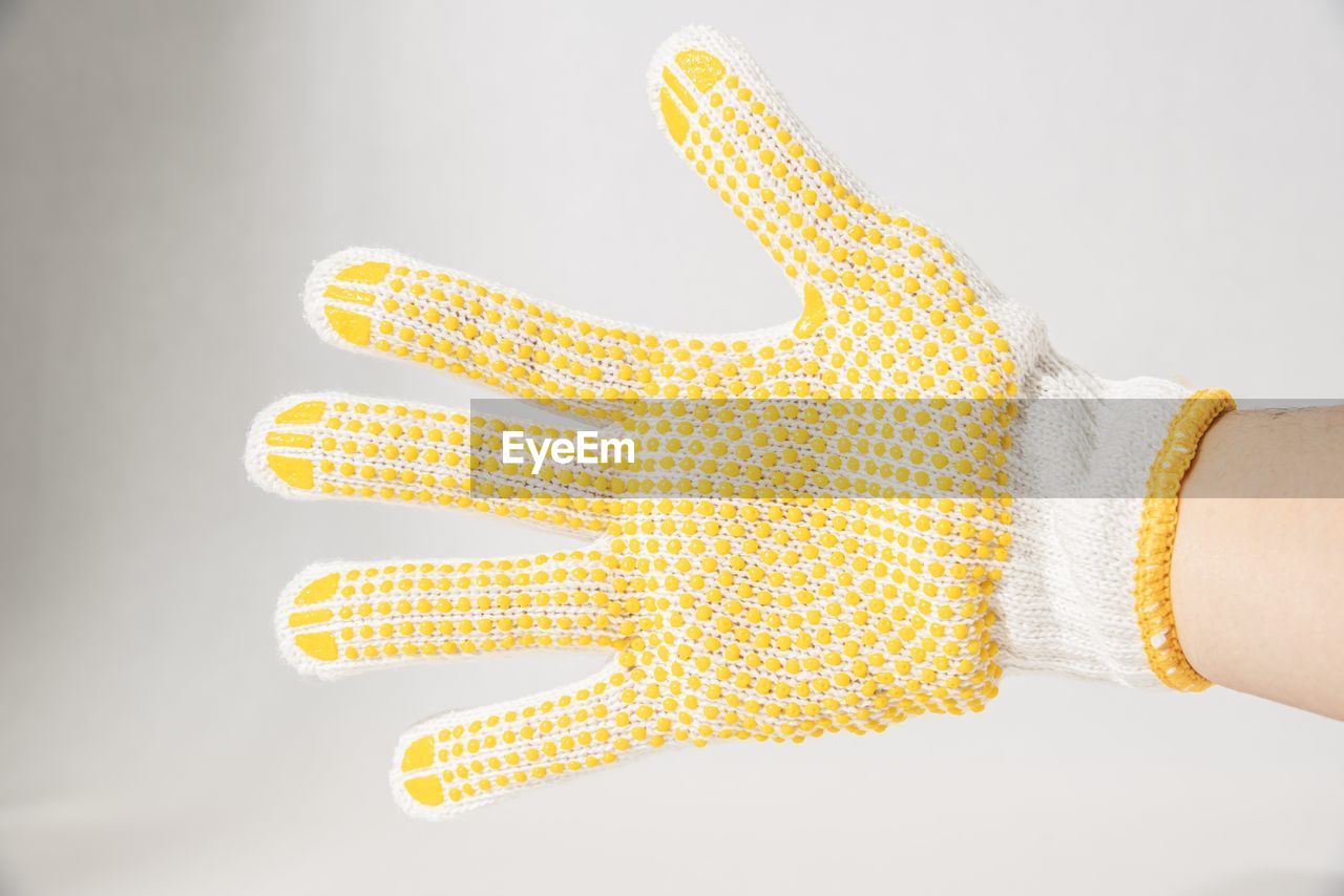 Cropped hand of person wearing knit glove against white background