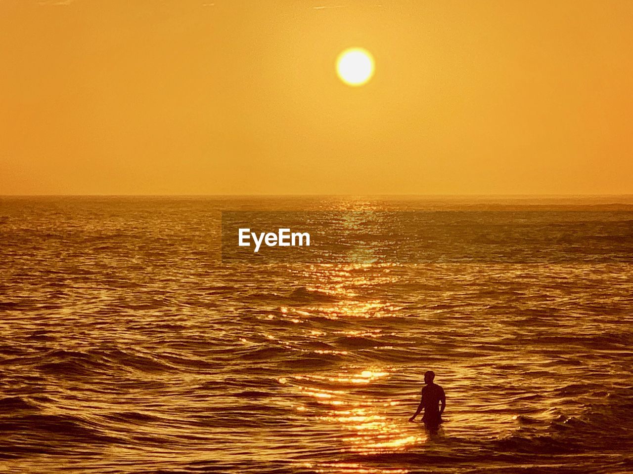 SILHOUETTE MAN IN SEA AGAINST ORANGE SKY