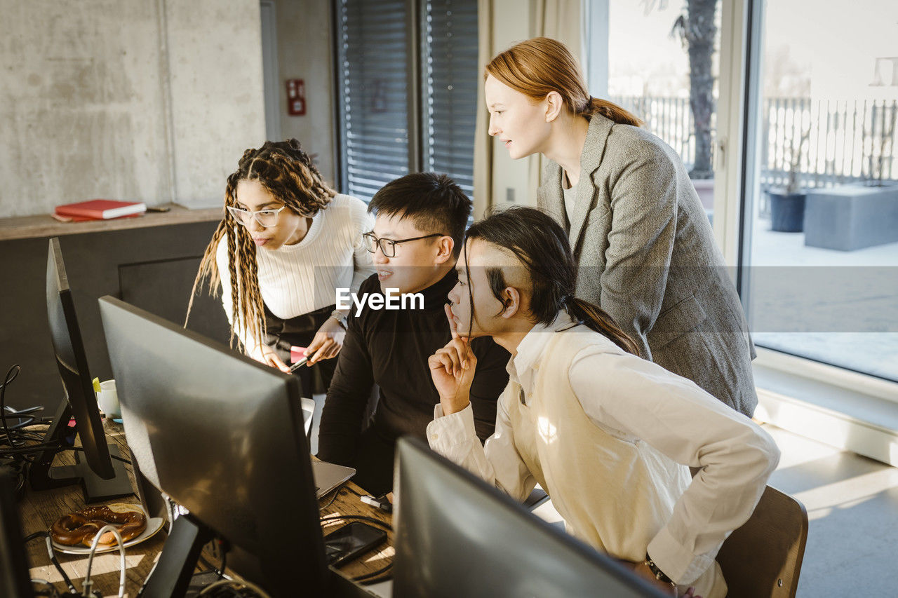 Multiracial male and female programmers discussing over computer in creative office