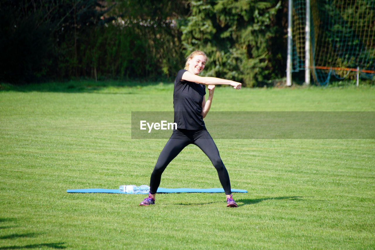 Smiling woman exercising on grassy field