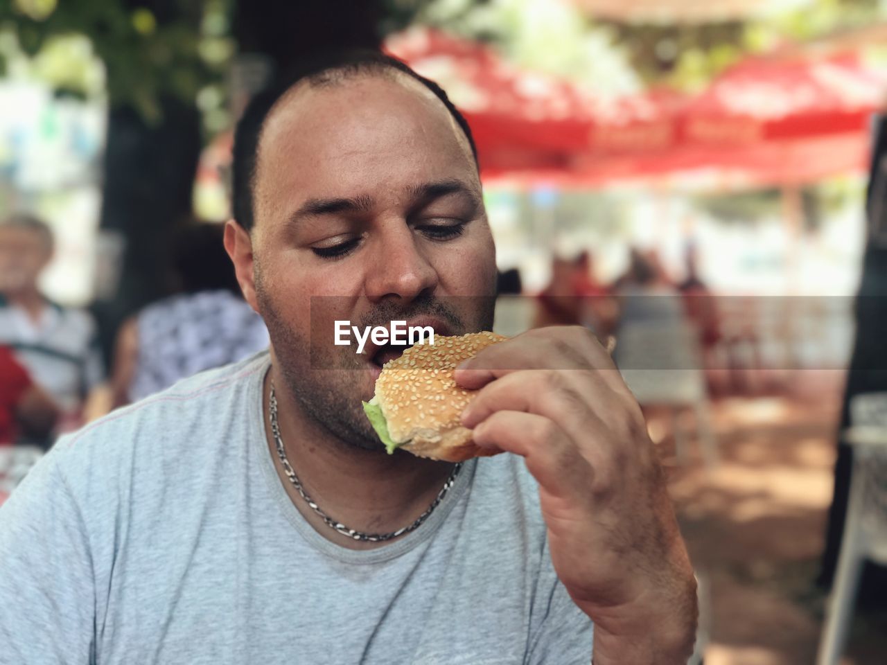 Close-up of mid adult man eating burger at sidewalk cafe