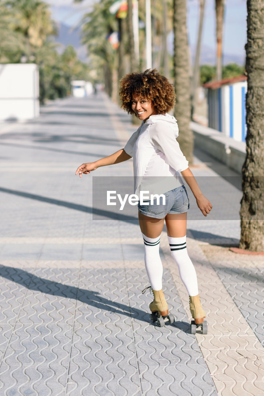 Rear view portrait of woman roller skating on sidewalk in city