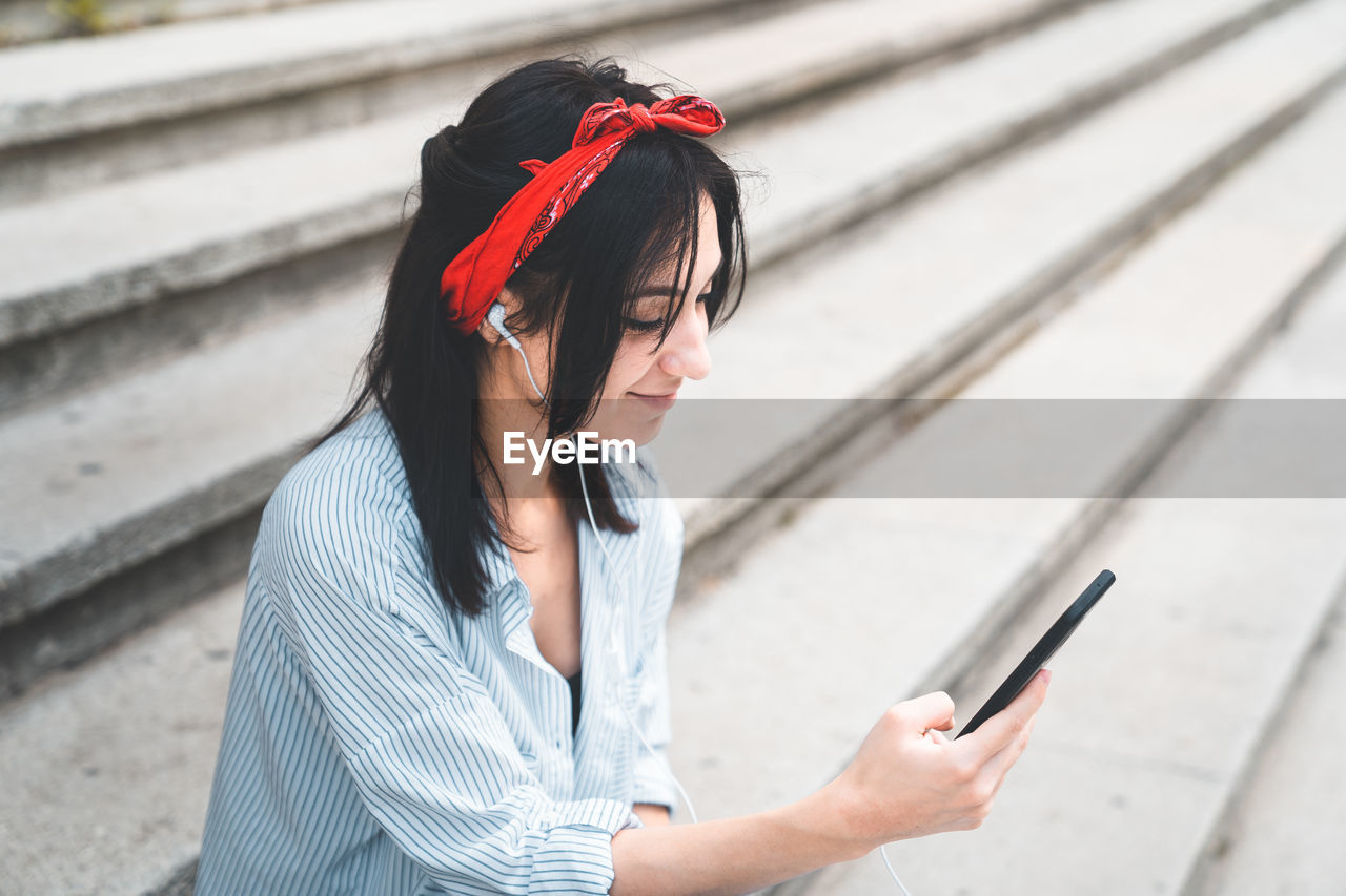 Young woman using phone while sitting on staircase