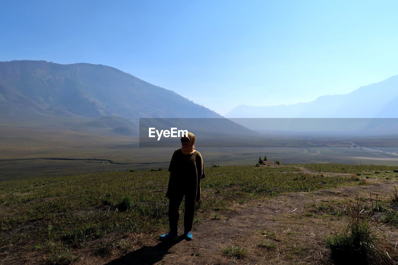 Woman standing on land against clear blue sky