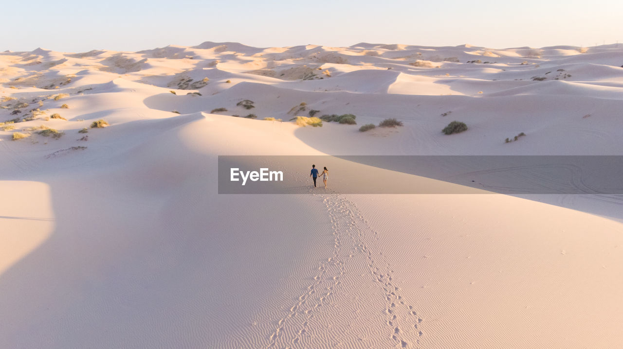 High angle view of couple walking on sand at desert against sky