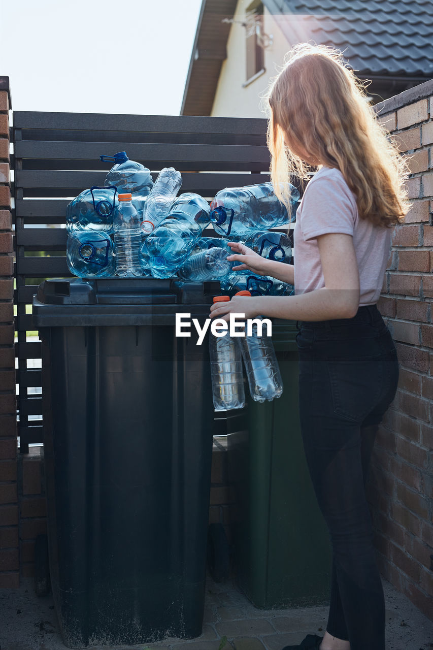 Side view of girl standing by garbage bin