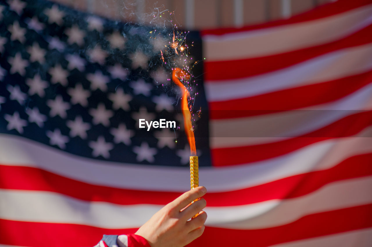 Close-up of hand holding firework against american flag