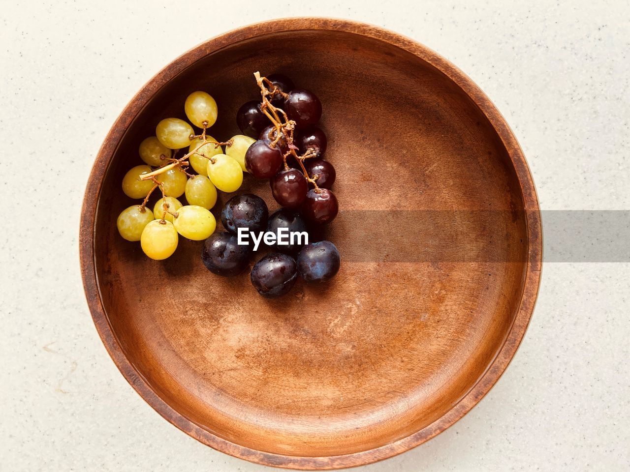 Plums and grapes in  wooden bowl. two bunches. red grapes, green grapes. purplish blue plums. 