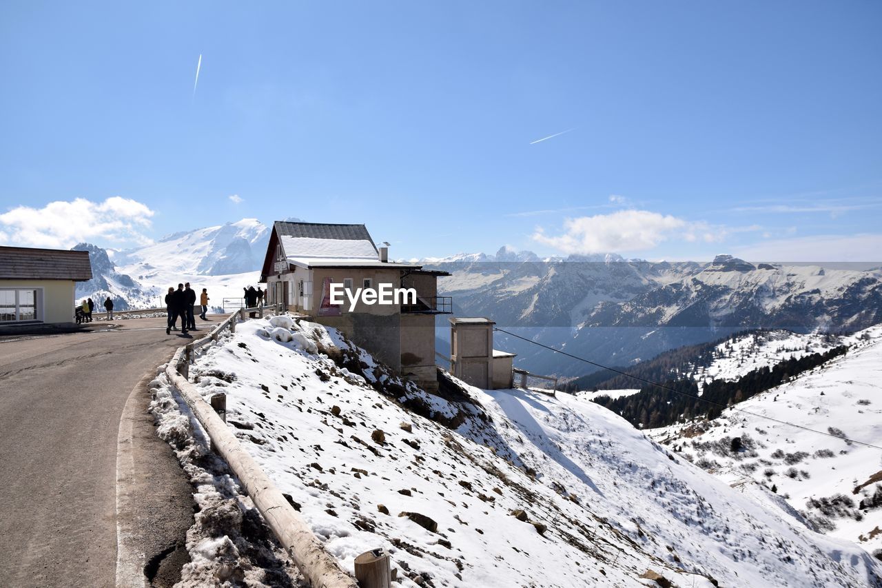 Log cabins on snow covered dolomites mountains against blue sky