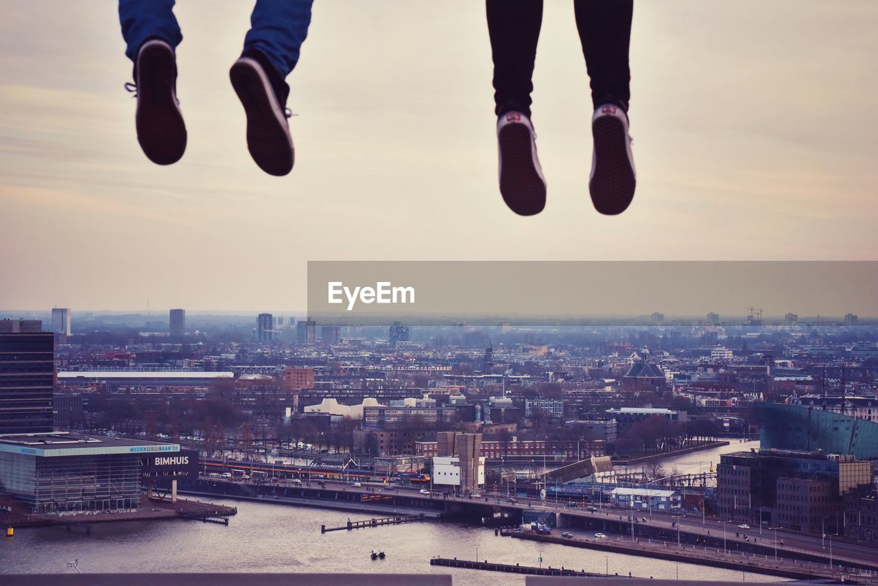 LOW SECTION OF PERSON WITH CITYSCAPE AGAINST SKY