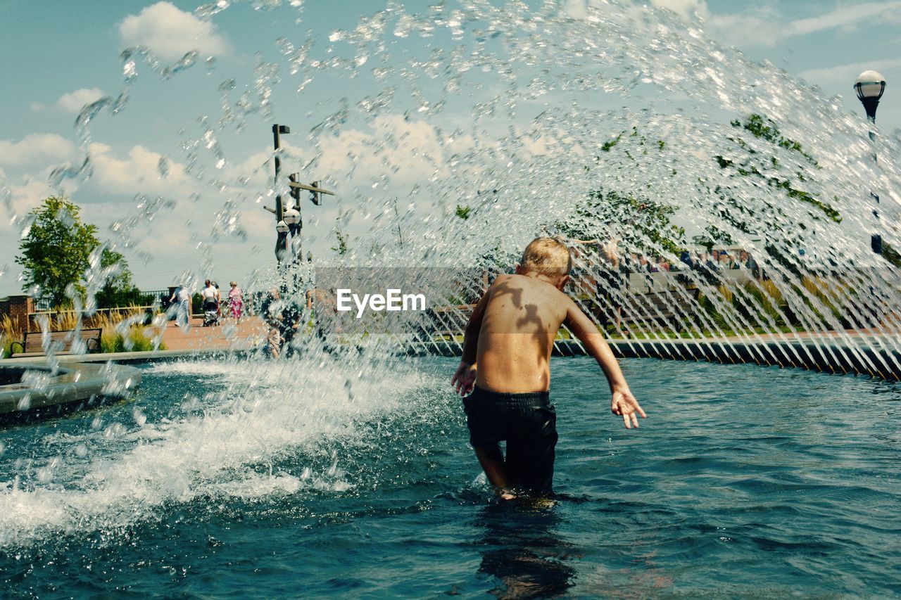 Rear view of shirtless boy enjoying fountain