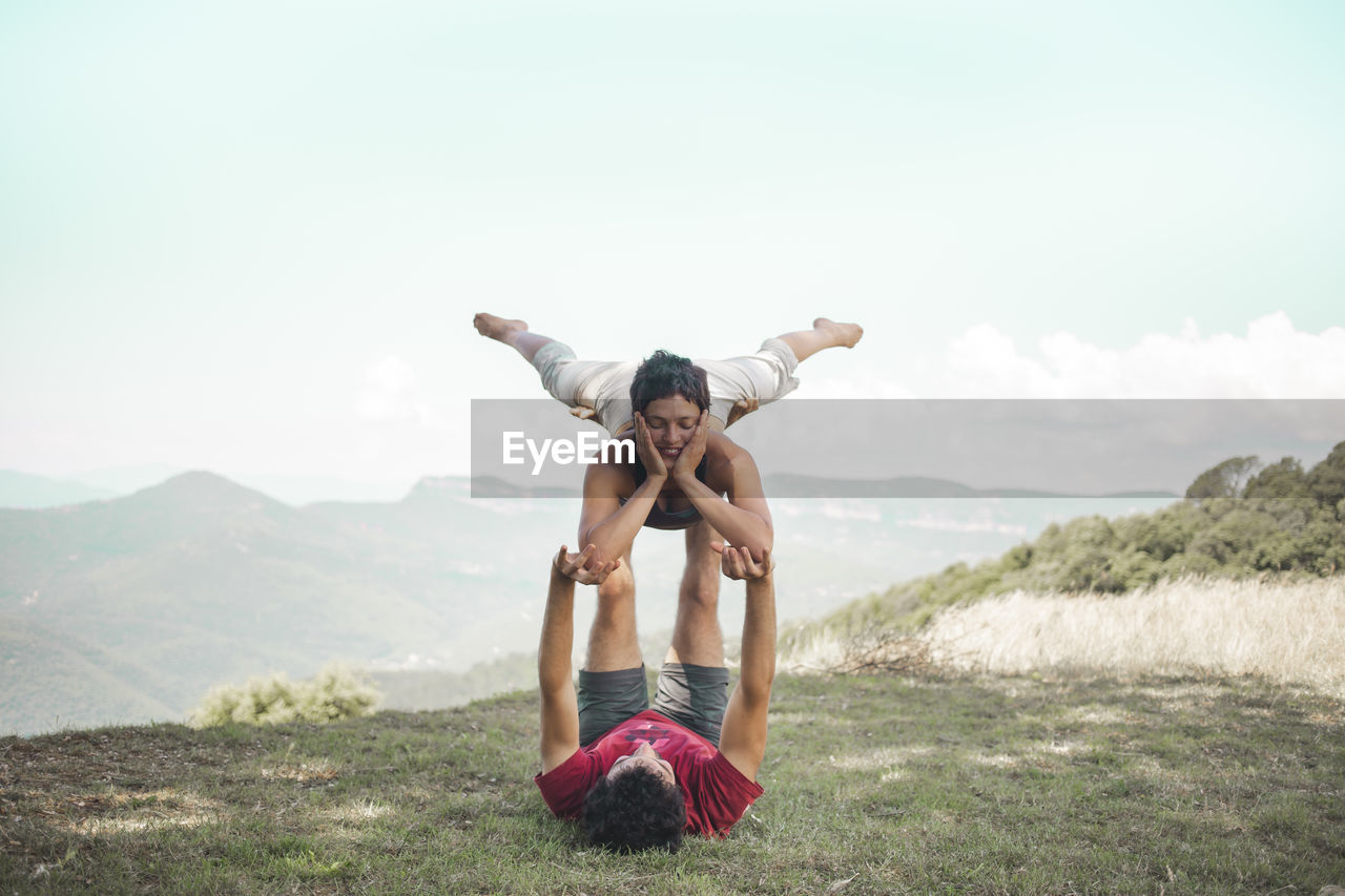 Couple doing acroyoga on mountain in front of sky