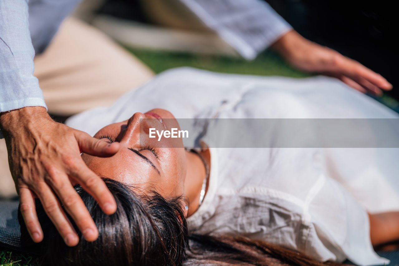 Close-up image of relaxed woman lying with her eyes closed and having reiki healing treatment 