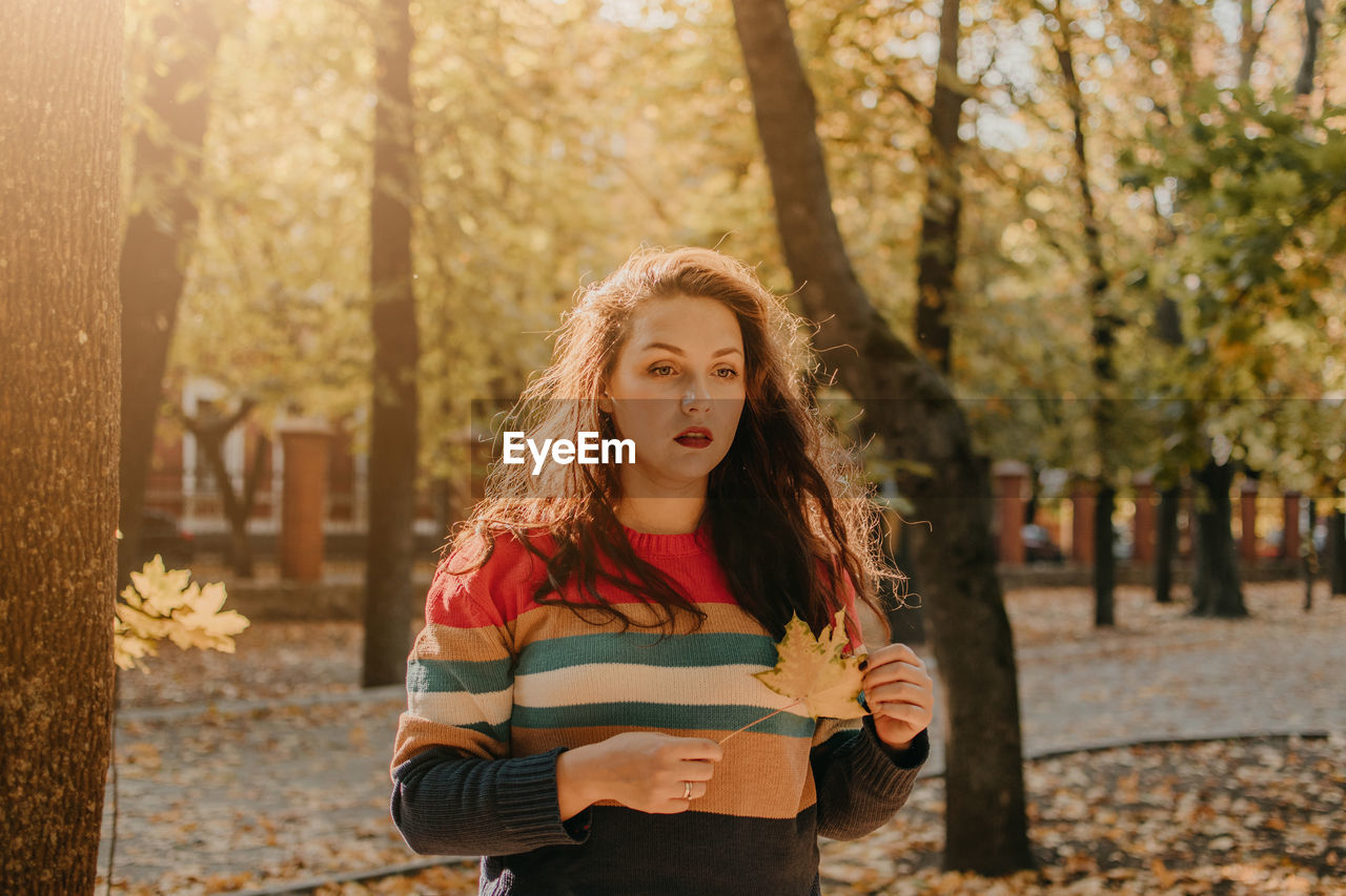 Portrait of young woman standing against tree