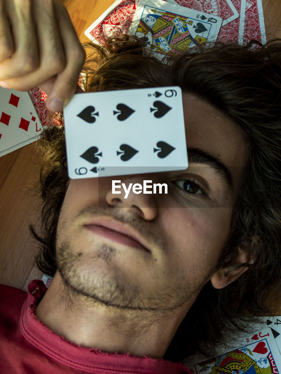 High angle view of man with playing cards lying on hardwood floor