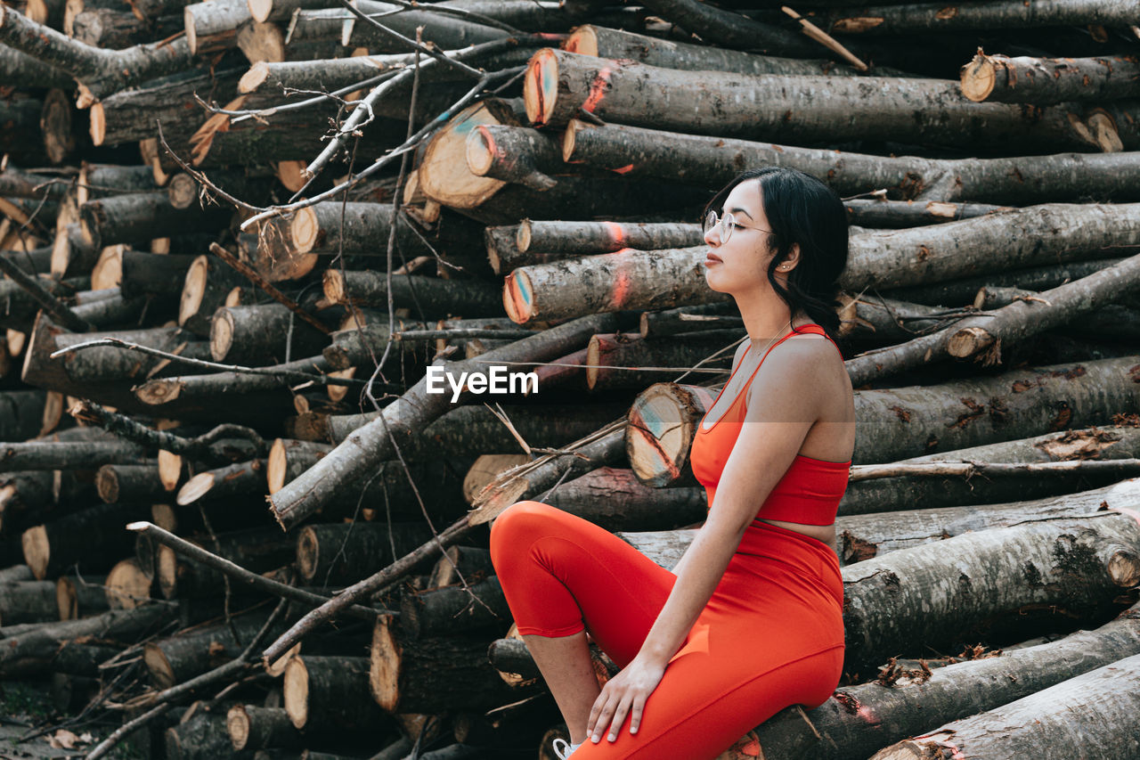 low angle view of young woman sitting on logs in forest