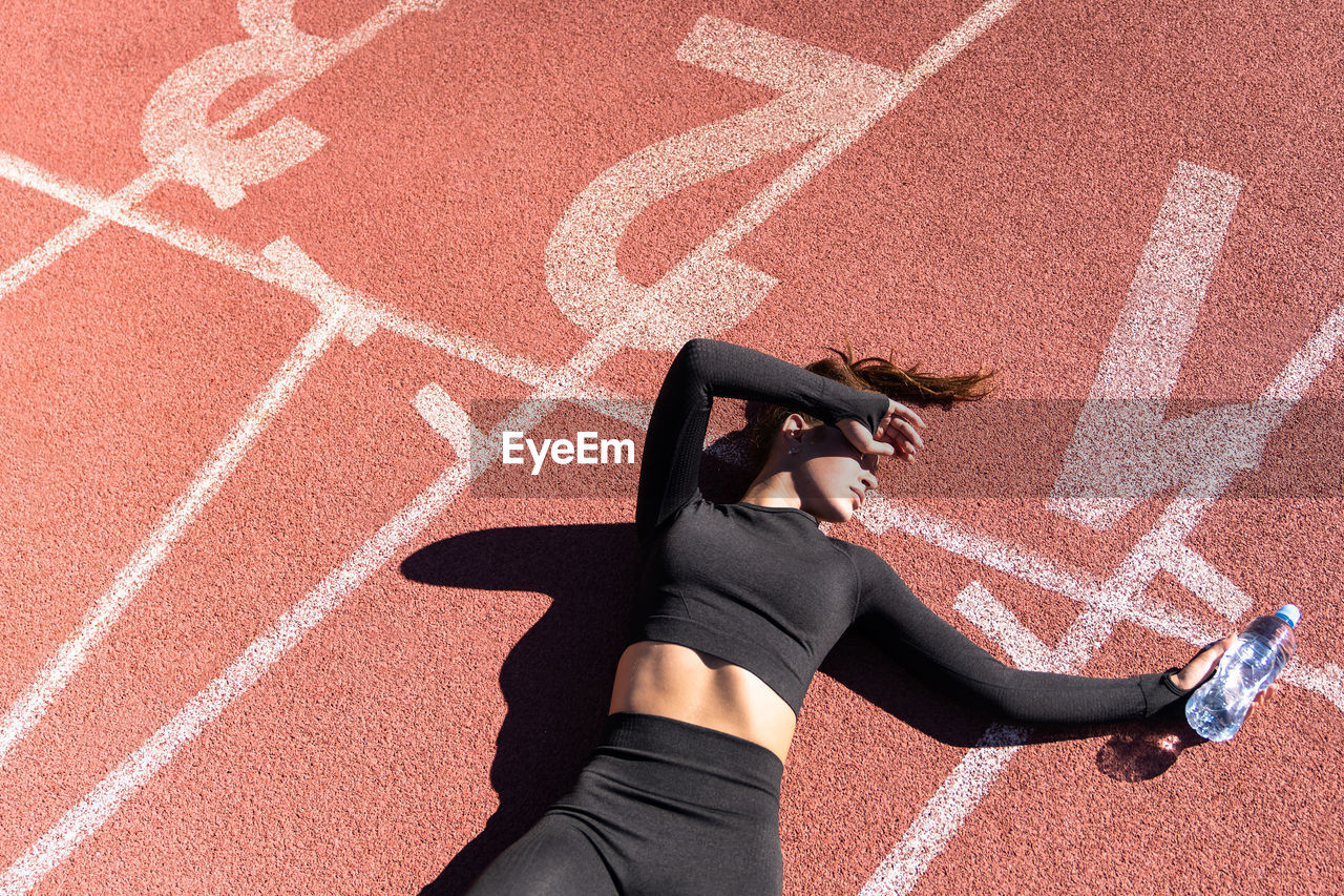 High angle view of tired woman lying with water bottle on running track