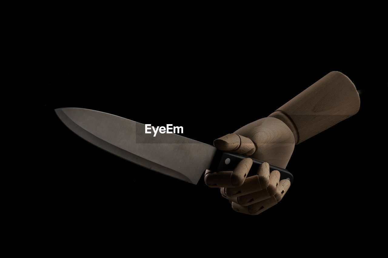Sharp knife in wooden hand in studio on black background demonstrating concept of violence