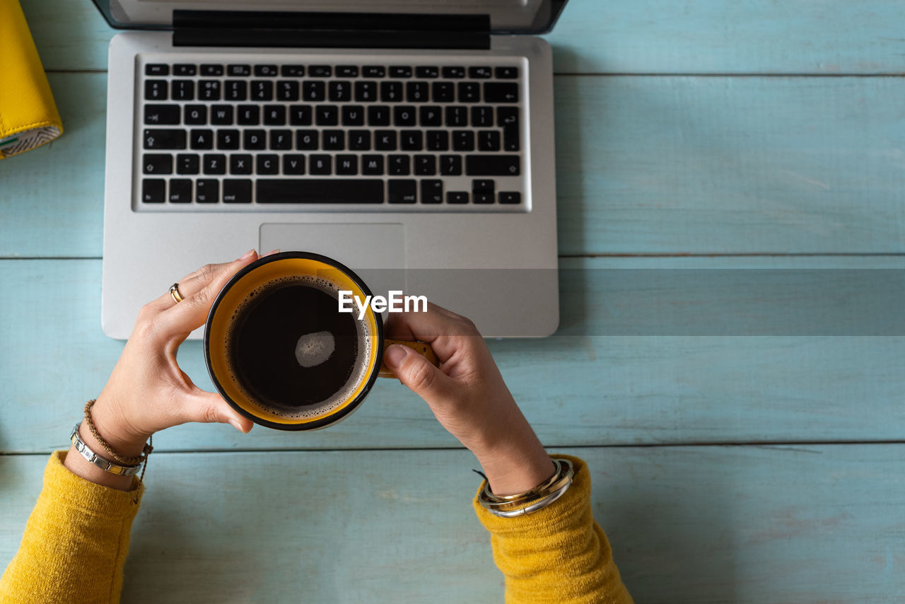 Top view of a woman's hands with a cup of coffee and a laptop computer. copy space