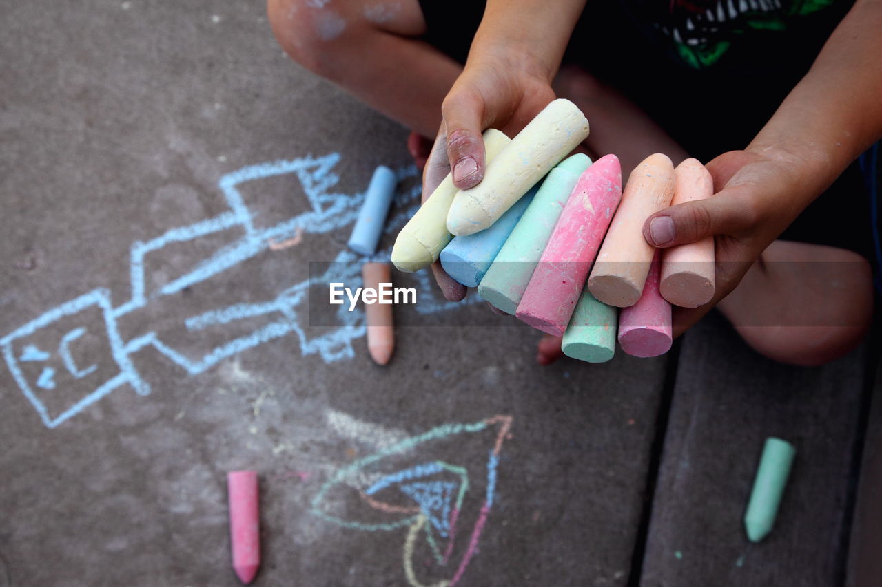 Low section of boy holding colorful chalks