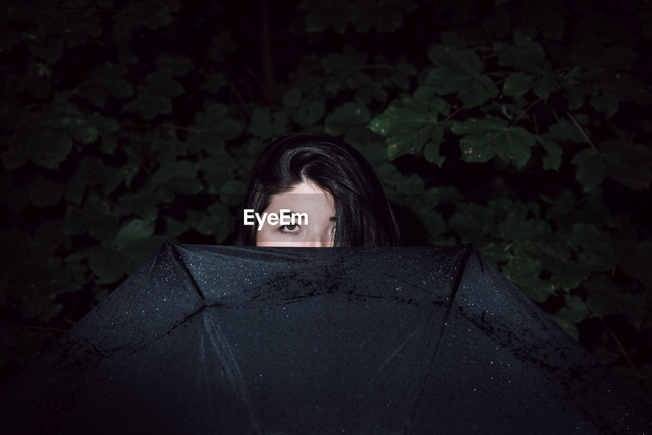 Portrait of woman with umbrella against tree at night