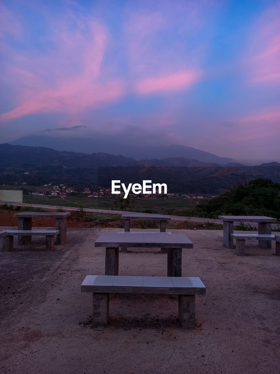 EMPTY BENCH AND TABLE AGAINST MOUNTAINS AT SUNSET