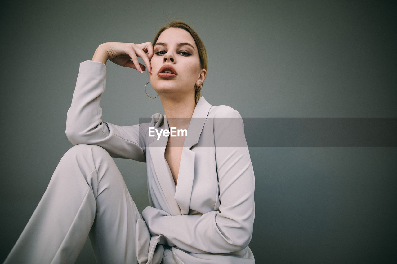 Portrait of young woman sitting against wall