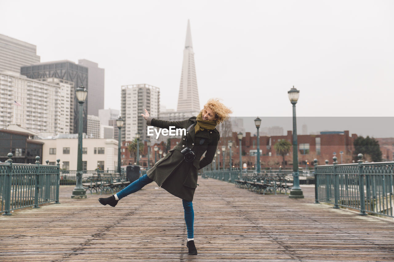 Woman dancing on bridge against buildings in city