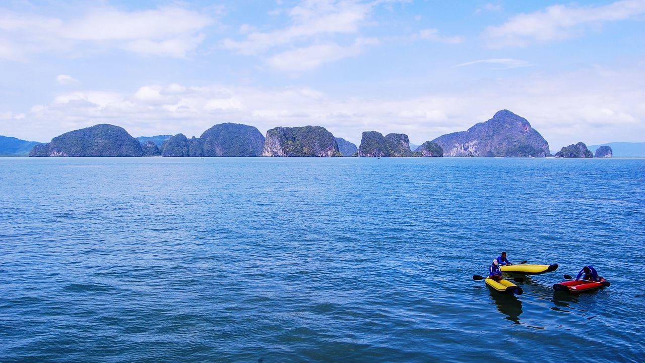 PEOPLE ON SEA BY MOUNTAIN AGAINST SKY