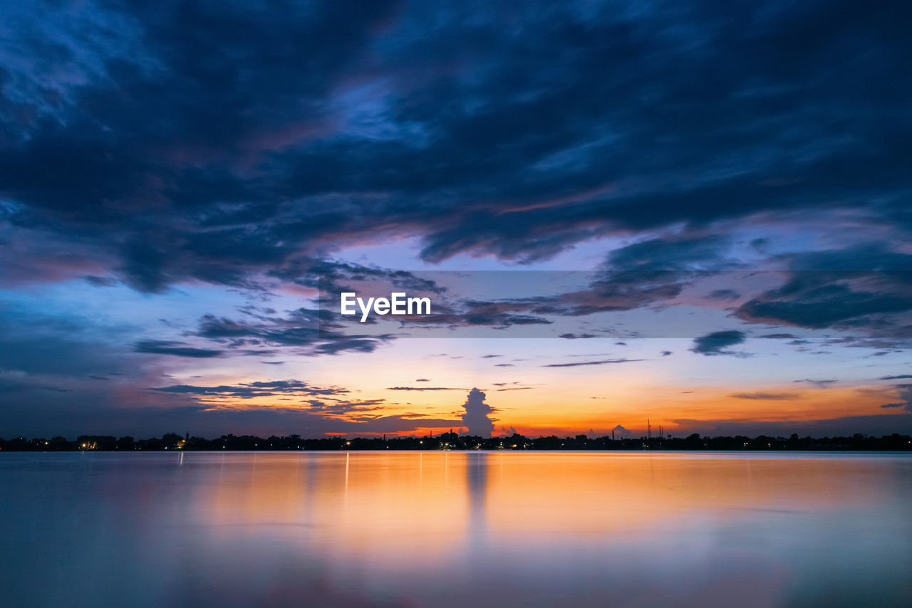 Scenic view of lake against dramatic sky during sunset